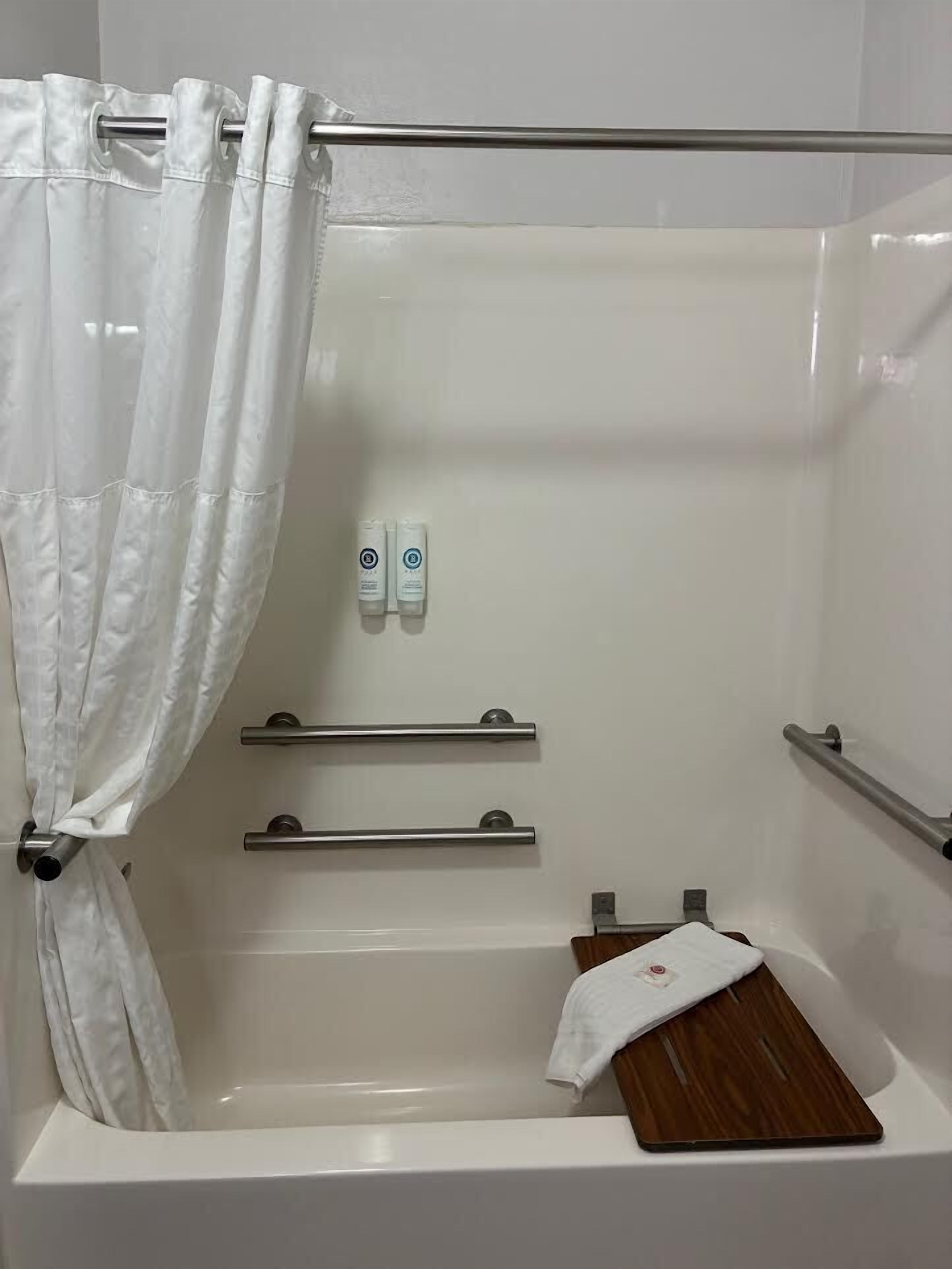 Un baño con bañera, cortina de ducha, dos dispensadores de gel hidroalcohólico y una bandeja de madera.