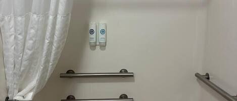 Un baño con bañera, cortina de ducha, dos dispensadores de gel hidroalcohólico y una bandeja de madera.