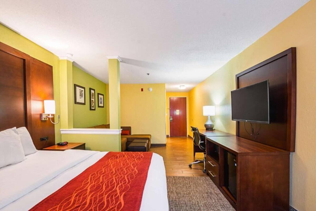 A hotel room with a bed, desk, television, and a door leading to another room.