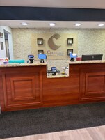 Una recepción de hotel con un muro de ladrillo, un letrero grande de 'Comfort Inn & Suites' y una laptop Dell en el mostrador.