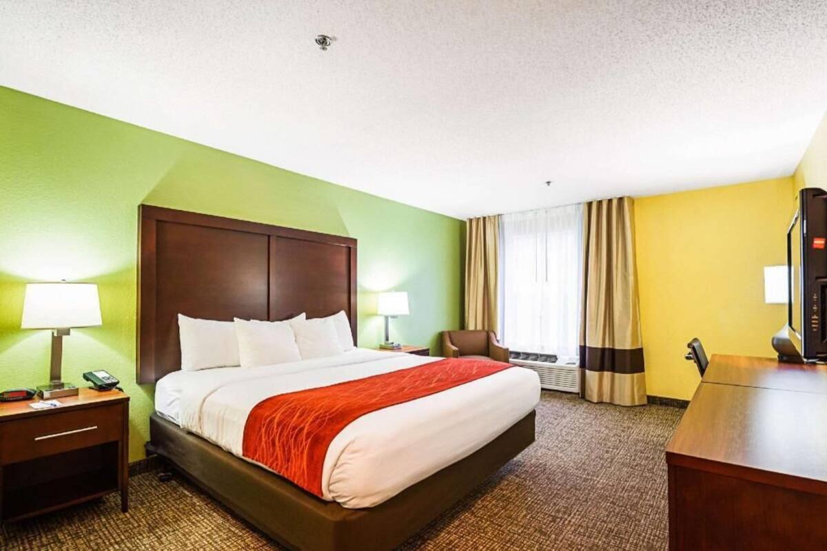 A hotel room with a large bed, a desk, a chair, and a window with curtains.