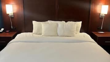 A large bed with white linens and pillows, flanked by wooden headboards and bedside tables with lamps.