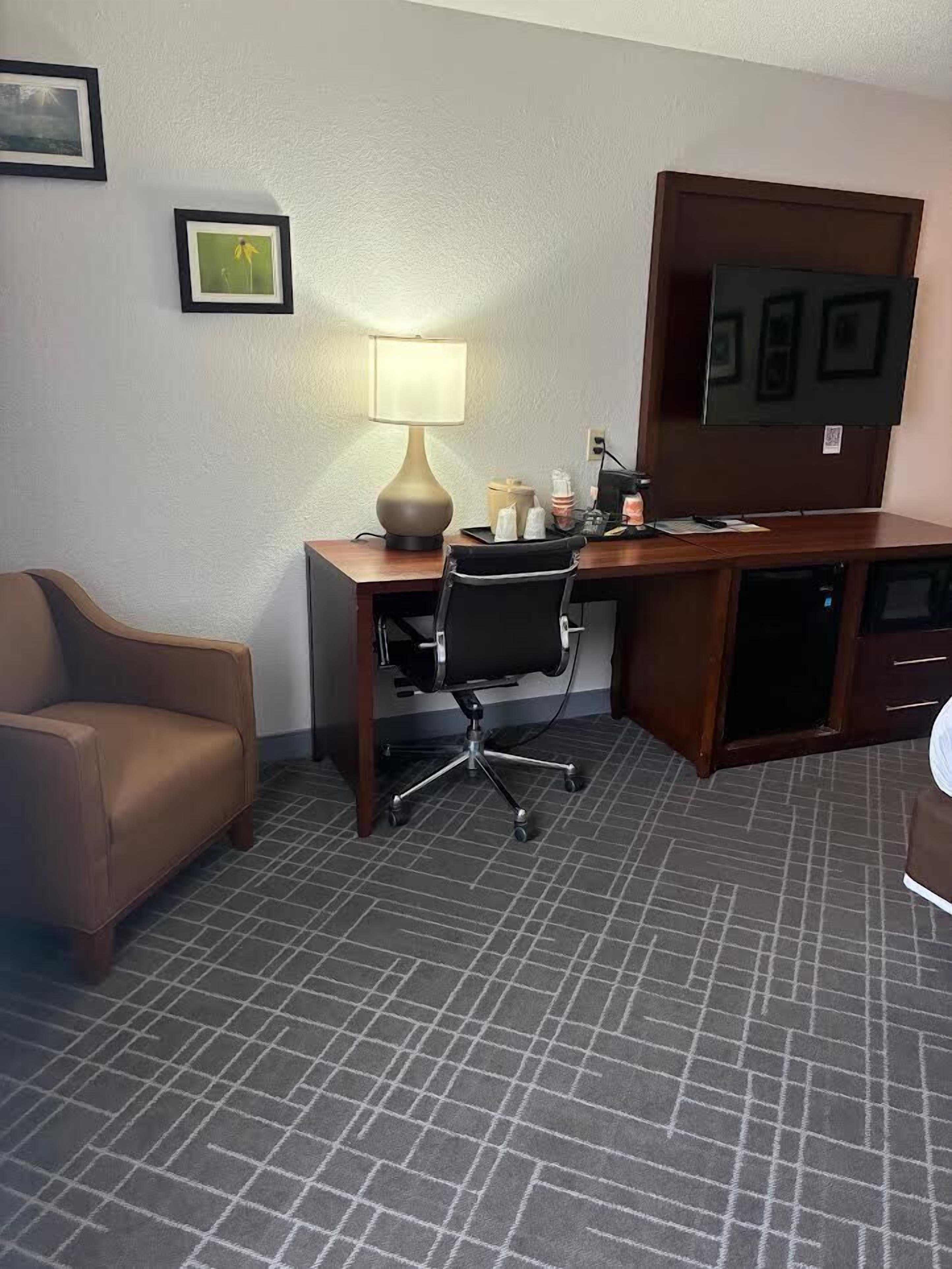 A hotel room with a desk, chair, lamp, and a television.
