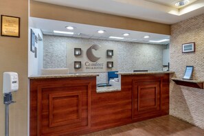 A reception desk with a sign reading "Comfort Inn & Suites," a brick-patterned wall, and a wooden counter. - Comfort Inn & Suites Dayton Northwest - Englewood (Englewood)