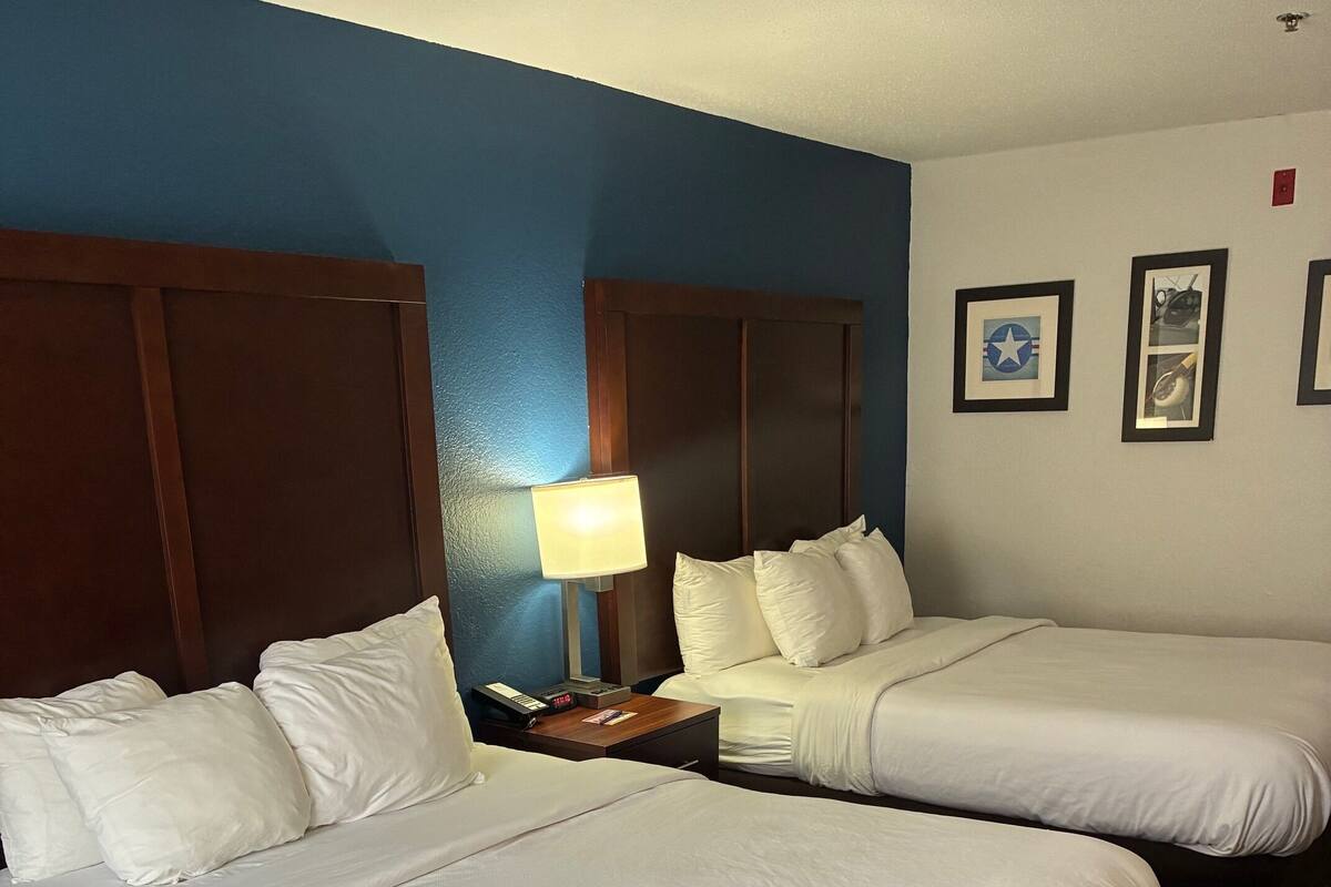 A hotel room with two beds, a nightstand with a lamp, and framed pictures on the wall.