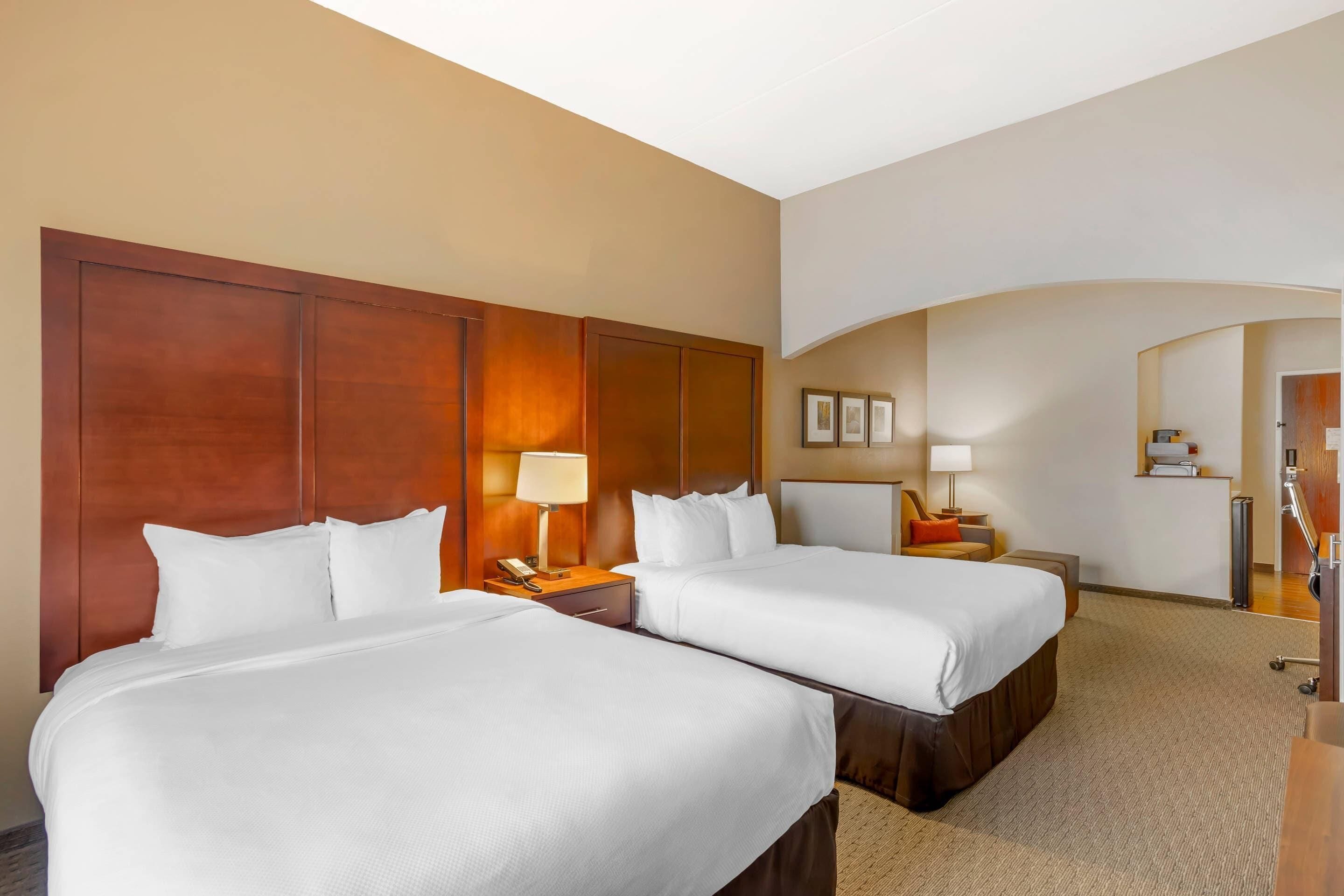 A hotel room with two beds, a wooden headboard, a desk with a lamp, and a small seating area.