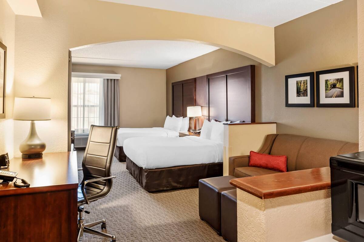 A hotel room with a desk, two beds, a sofa, and a fireplace.