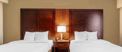 A hotel room with two beds, a nightstand with a lamp, and a wooden headboard.