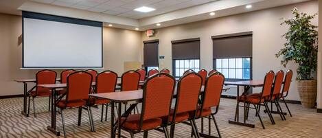 A conference room with a large projection screen, multiple tables with chairs, and a carpeted floor.