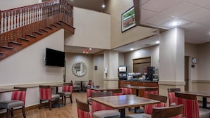 A hotel lobby with a staircase, seating areas, a clock, a TV, and a coffee station. - Comfort Suites State College near Penn State (State College)