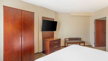 Habitación de hotel con una cama grande, un armario de madera, un televisor montado en la pared, una mesita y una puerta.