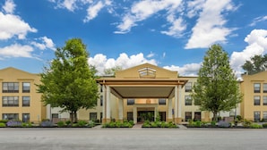 A hotel with a covered entrance, multiple floors, and a landscaped front yard with trees and shrubs. - Comfort Suites State College near Penn State (State College)