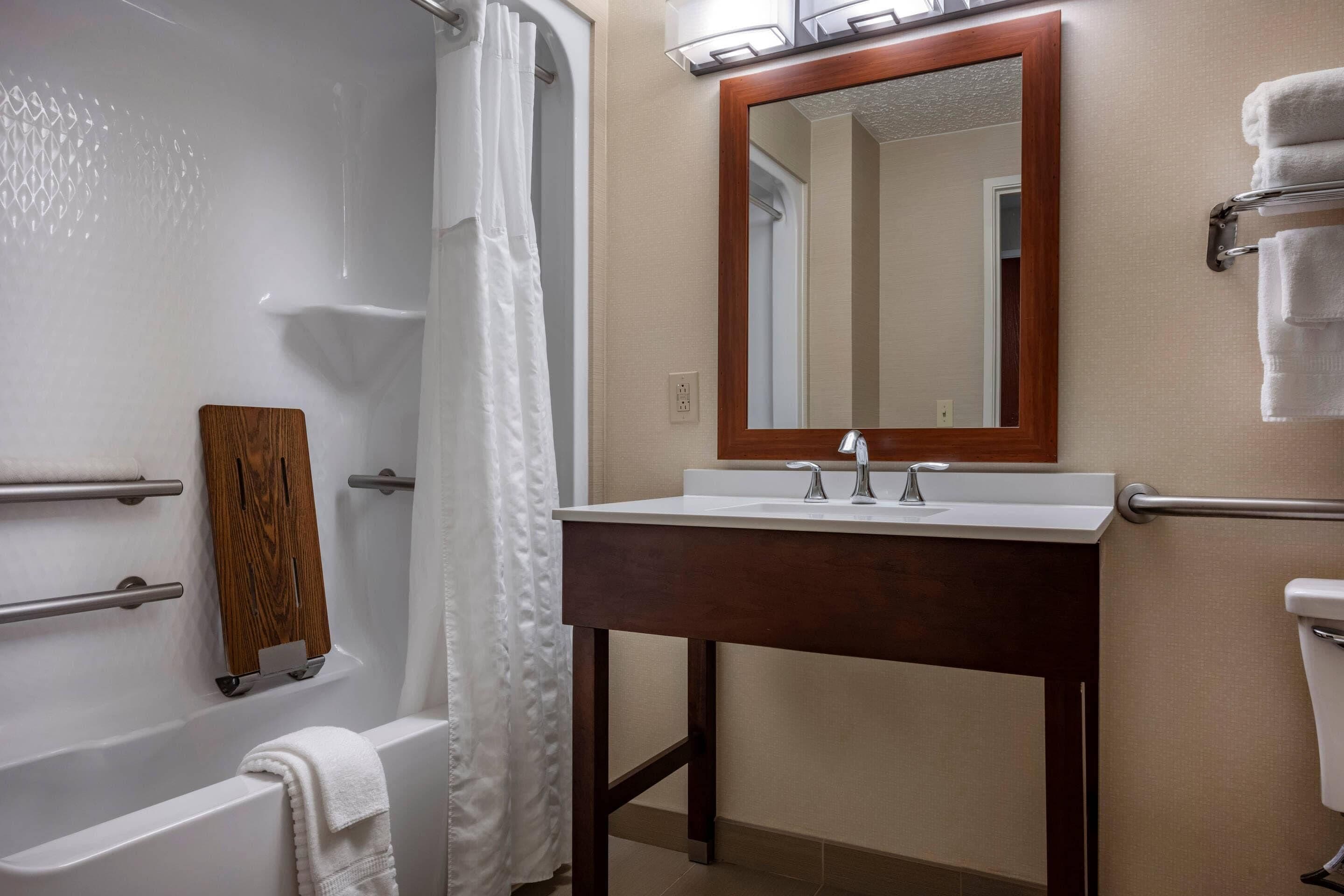A bathroom with a bathtub, a wooden shelf, a sink with a mirror, and a towel rack.