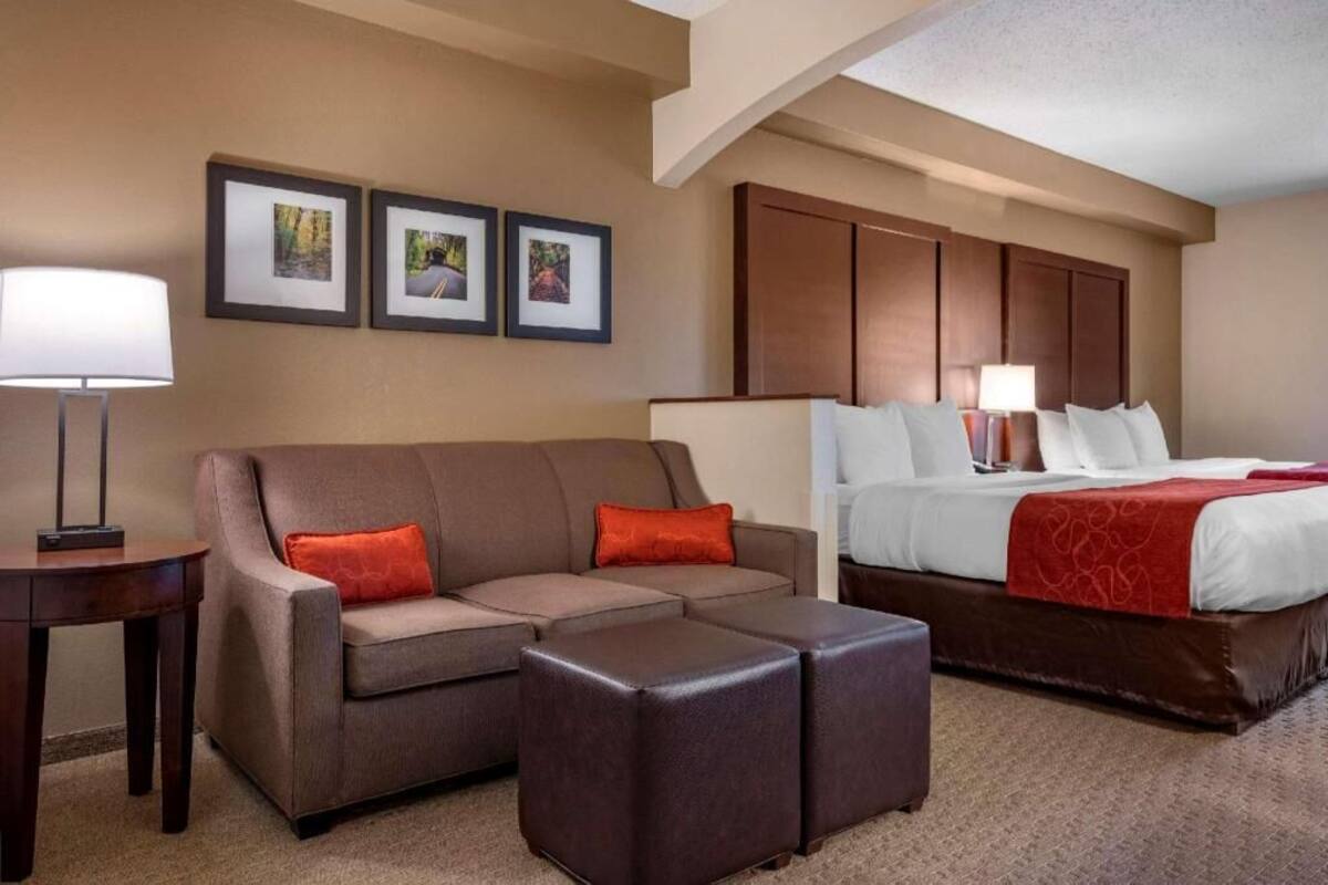 A hotel room with a sofa, ottoman, bed, and two bedside tables.