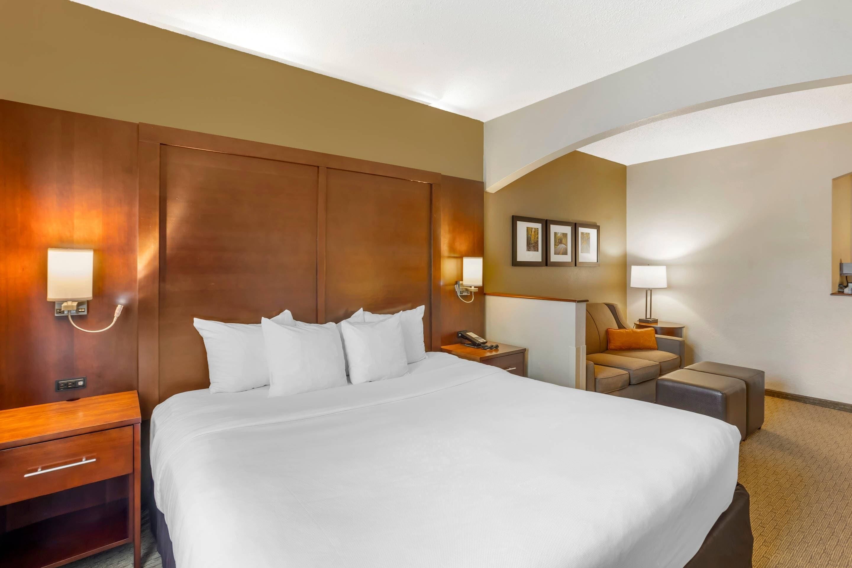 A hotel room with a large bed, bedside tables, a desk, a chair, and a sofa.