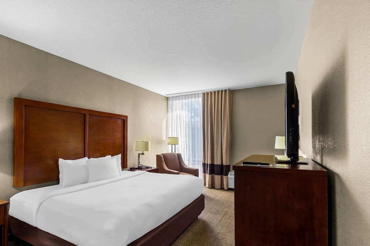 A hotel room with a large bed, a desk with a computer, a chair, and a television.