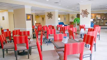A spacious indoor dining area with multiple tables and red upholstered chairs.