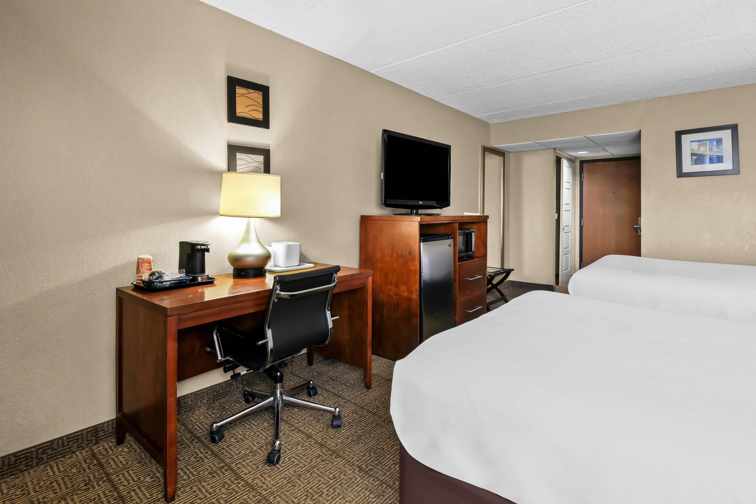 Une chambre d’hôtel comprenant un lit, un bureau avec une chaise, une télévision, un réfrigérateur et une lampe.