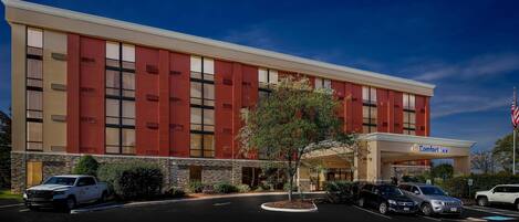 A Comfort Inn hotel with a modern facade, parking lot, and an American flag.