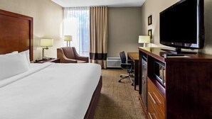 Habitació d'hotel amb un llit gran, una taula de treball amb televisió de pantalla plana, una cadira, una làmpada de taula i una finestra amb cortines.