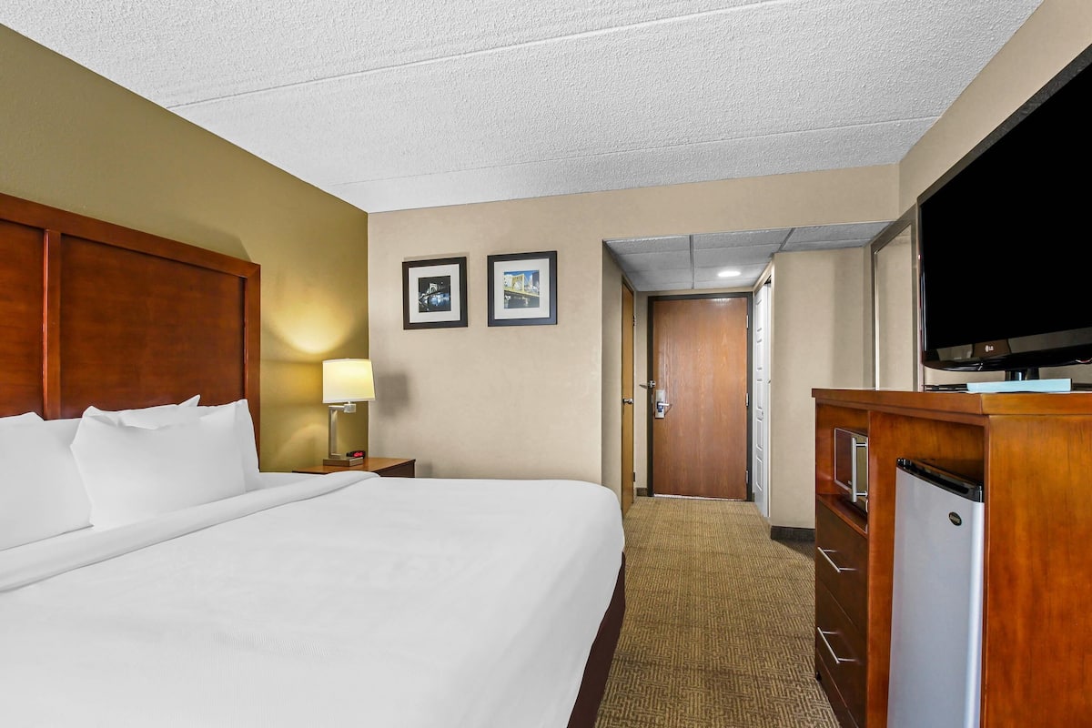 A hotel room with a large bed, a television, a desk with a computer, and a door leading to another room.