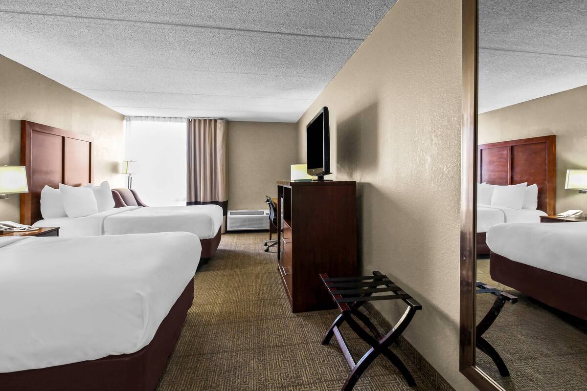 A hotel room with two beds, a desk, a television, and a mirror.
