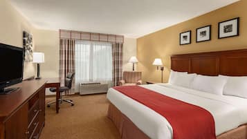 Habitación de hotel con cama, escritorio con televisor, una silla, ventana con cortinas y tres cuadros en la pared.