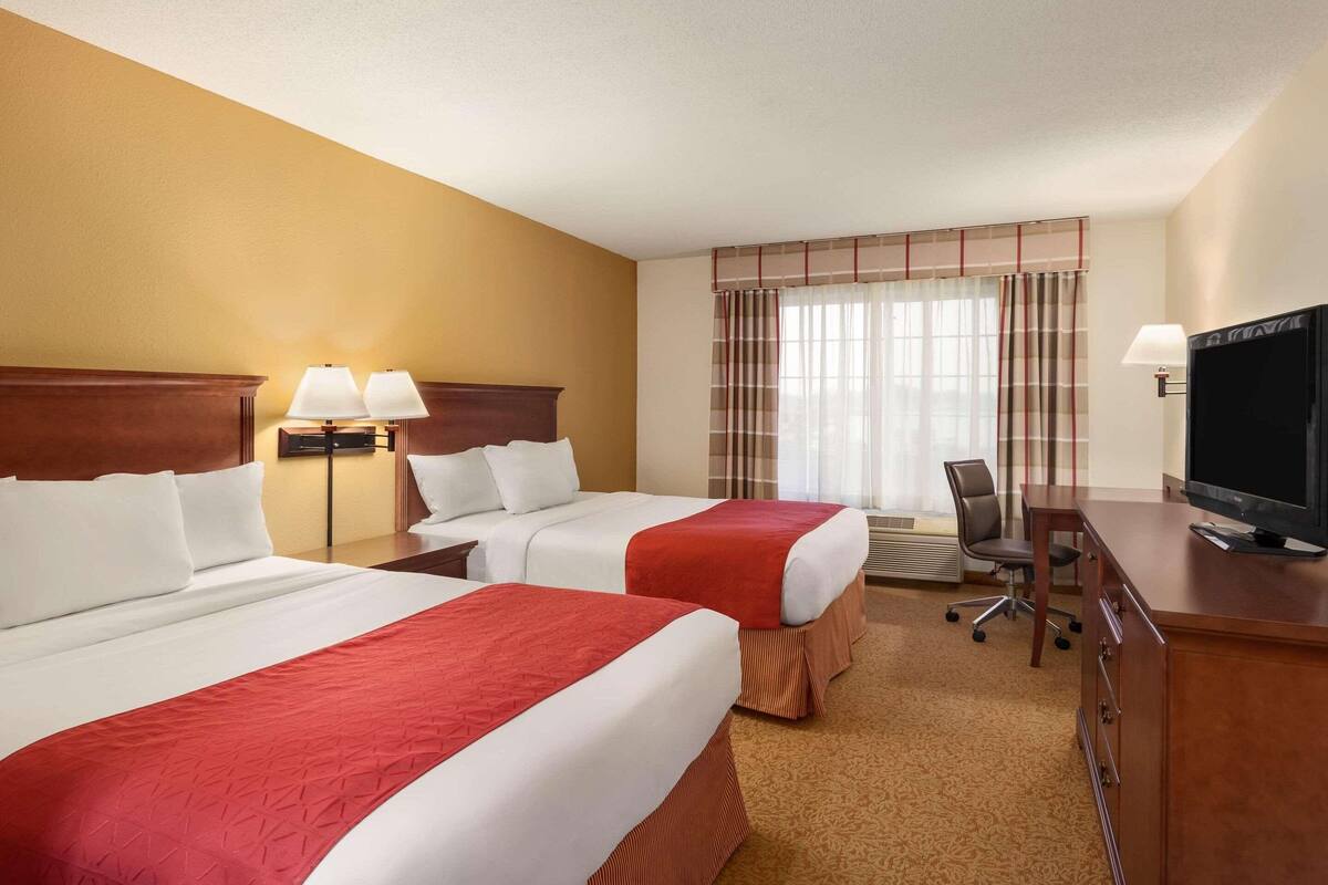A hotel room with two beds, a desk with a television, and a window with curtains.