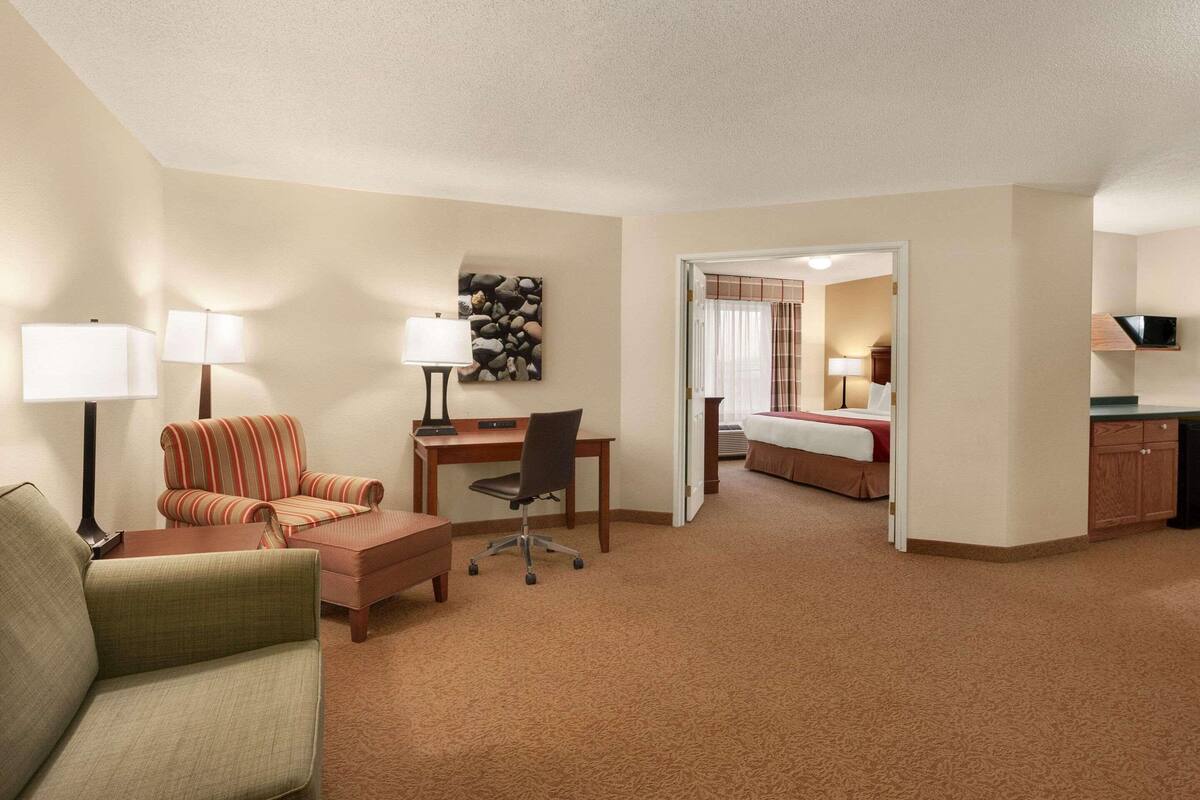 A hotel room with a sofa, a desk, a chair, a bed, and a television.