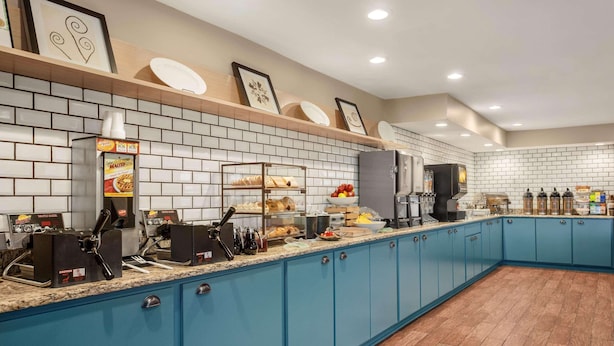 A kitchen area with blue cabinets, a coffee station, and a display of food items. - Country Inn & Suites by Radisson, Ames, IA (Ames)