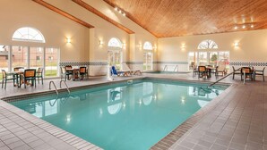 A swimming pool with lounge chairs and tables, surrounded by tiled walls and wooden beams. - Country Inn & Suites by Radisson, Ames, IA (Ames)