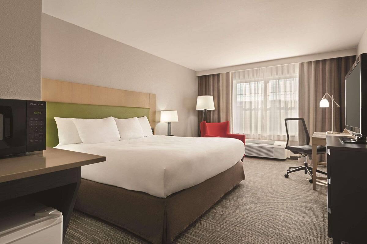 A hotel room with a bed, a desk, a chair, a TV, a lamp, and a window with curtains.