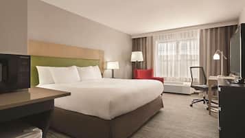 A hotel room with a bed, a desk, a chair, a TV, a lamp, and a window with curtains.