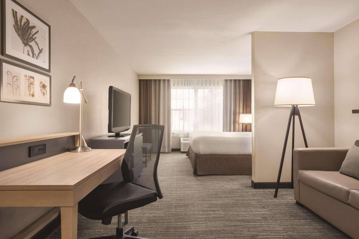 A hotel room with a desk, chair, bed, and two lamps.