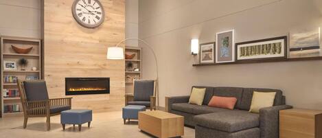 A modern living room with a fireplace, a clock, and a sofa with cushions.