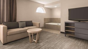A modern hotel room with a sofa, a small round table, a television, a bathtub, and a TV stand. - Country Inn & Suites by Radisson, Dubuque, IA (Dubuque)