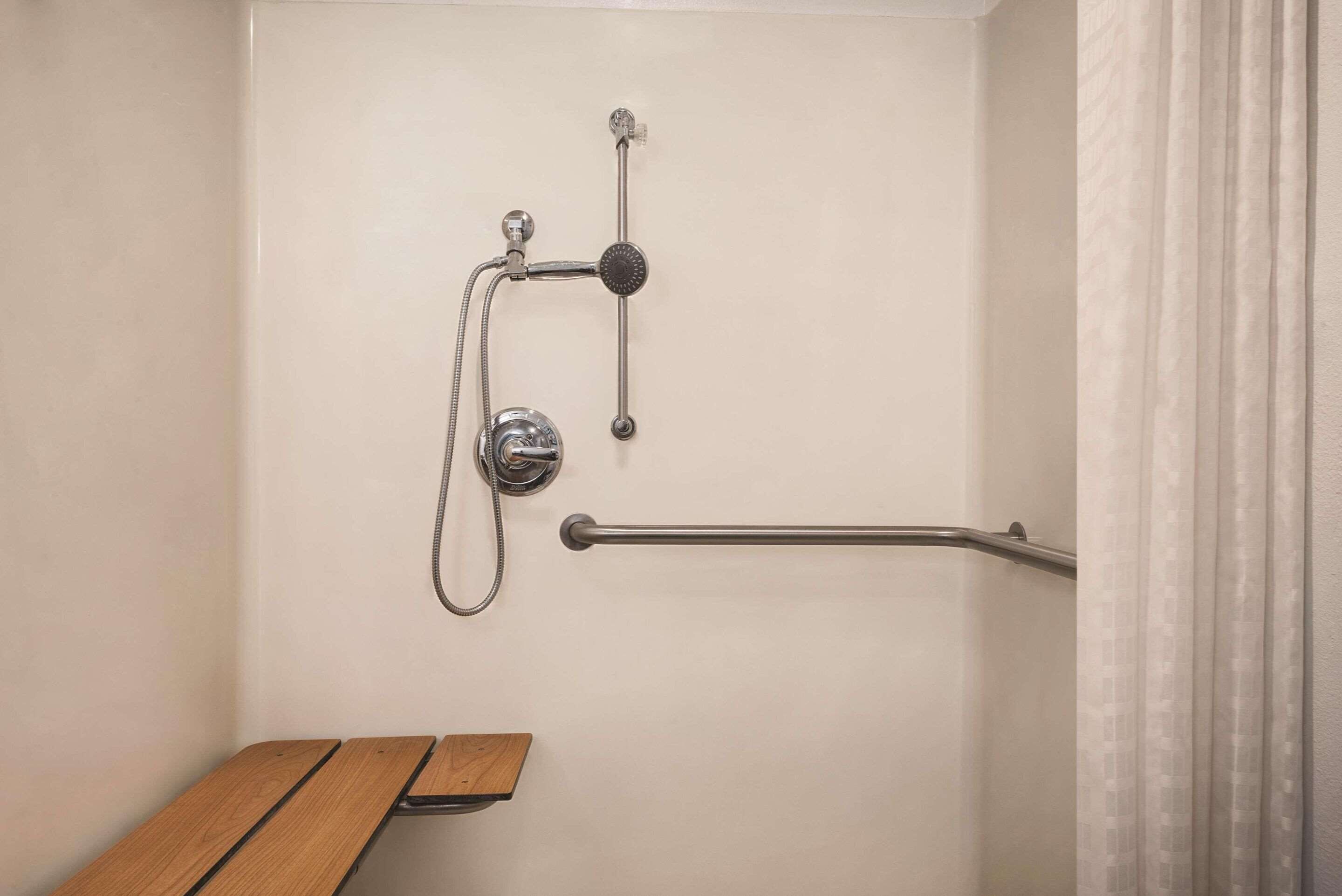 A shower area with a grab bar, a handheld showerhead, and a bench.