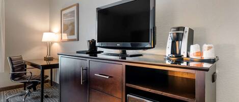 Habitación de hotel con televisión de pantalla plana, cafetera, microondas, escritorio con silla y un cuadro en la pared.