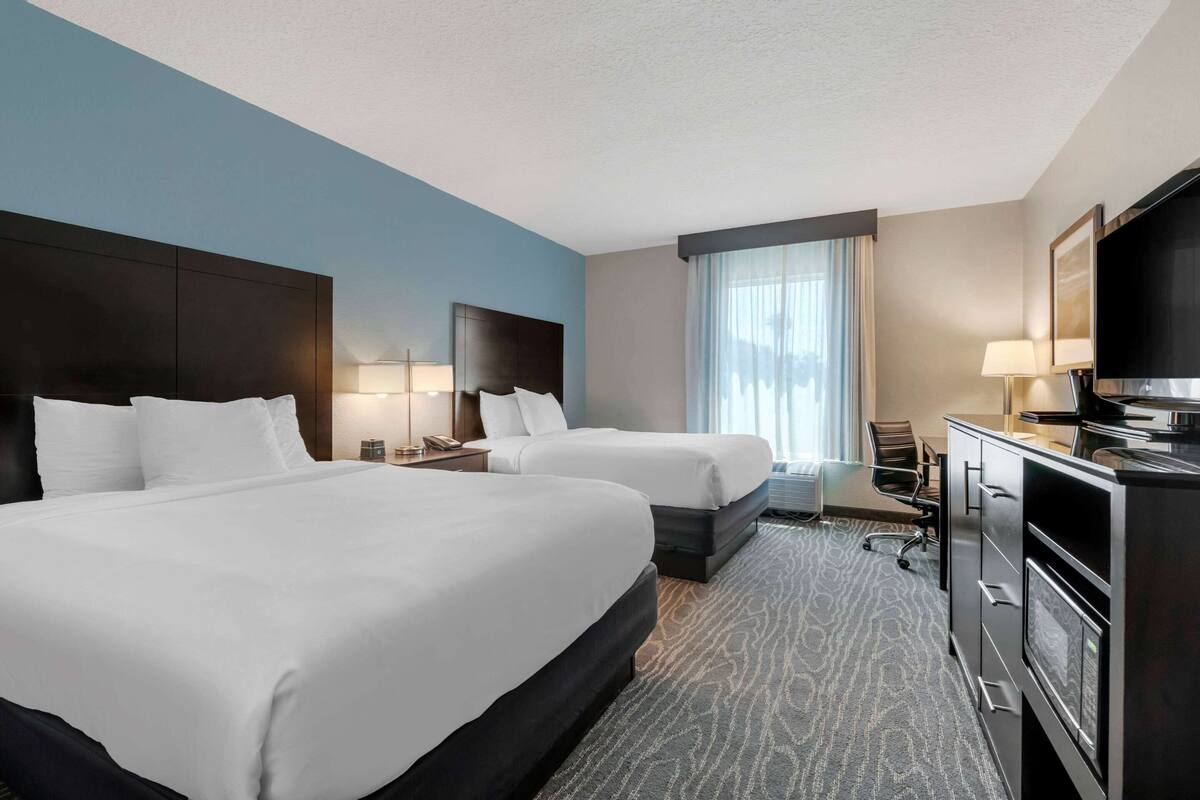 A hotel room with two beds, a desk, a television, and a window with curtains.