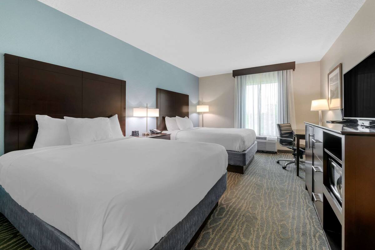 A hotel room with two beds, a desk, a chair, a television, and a window with curtains.
