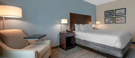 A hotel room with a bed, a chair, a nightstand, a lamp, and a wall with framed pictures.