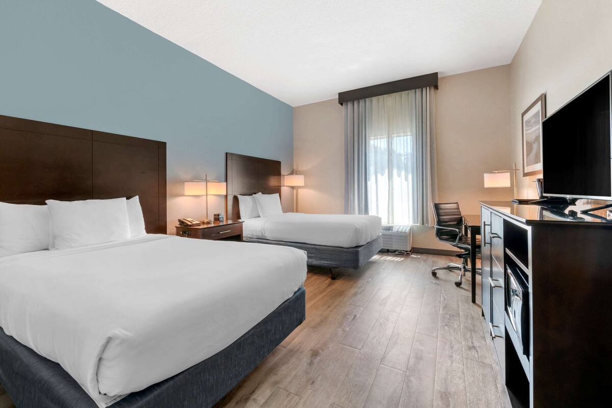 A hotel room with two beds, a desk, a chair, and a television.