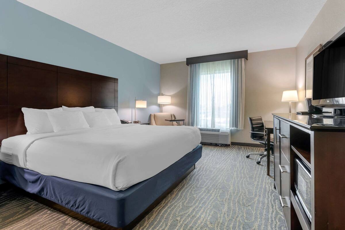 A hotel room with a large bed, a desk with a computer, a TV, and a minibar.