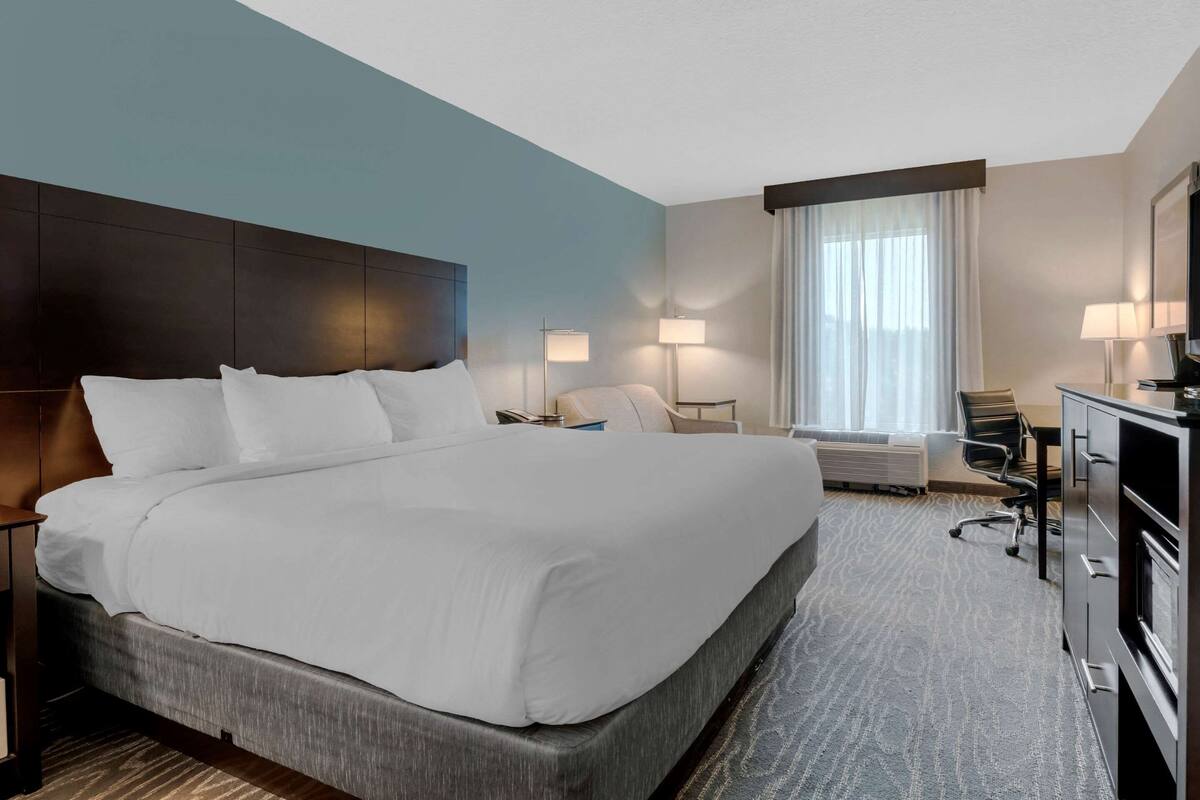 A hotel room with a large bed, a desk, a chair, a dresser, and a window with curtains.