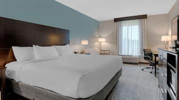 A hotel room with a large bed, a desk, a chair, a dresser, and a window with curtains.