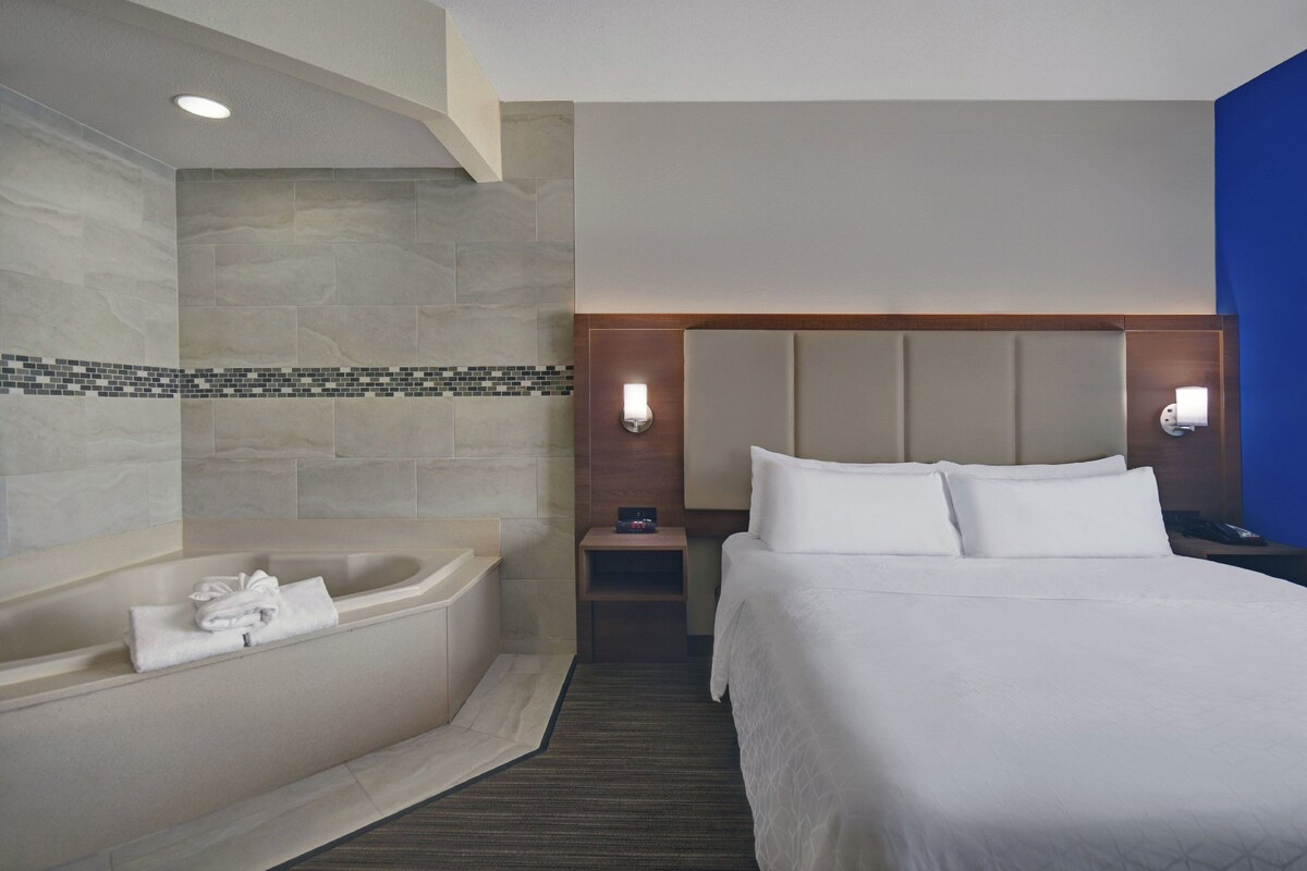 A hotel room with a large bed, a bathtub, and a nightstand with a lamp.