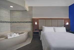 Habitación de hotel con una cama grande, una bañera y una mesita de noche con lámpara.
