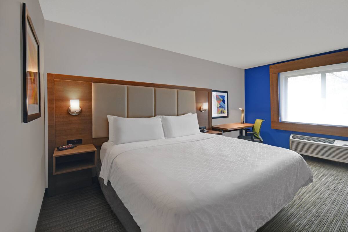 A hotel room with a large bed, bedside tables, a desk, and a window.