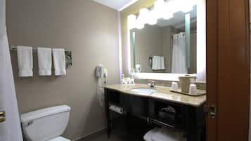 A bathroom with a toilet, sink, and mirror. There are towels hanging on the wall and a shower curtain.