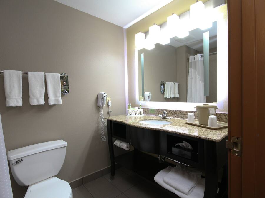 A bathroom with a toilet, sink, and mirror. There are towels hanging on the wall and a shower curtain.